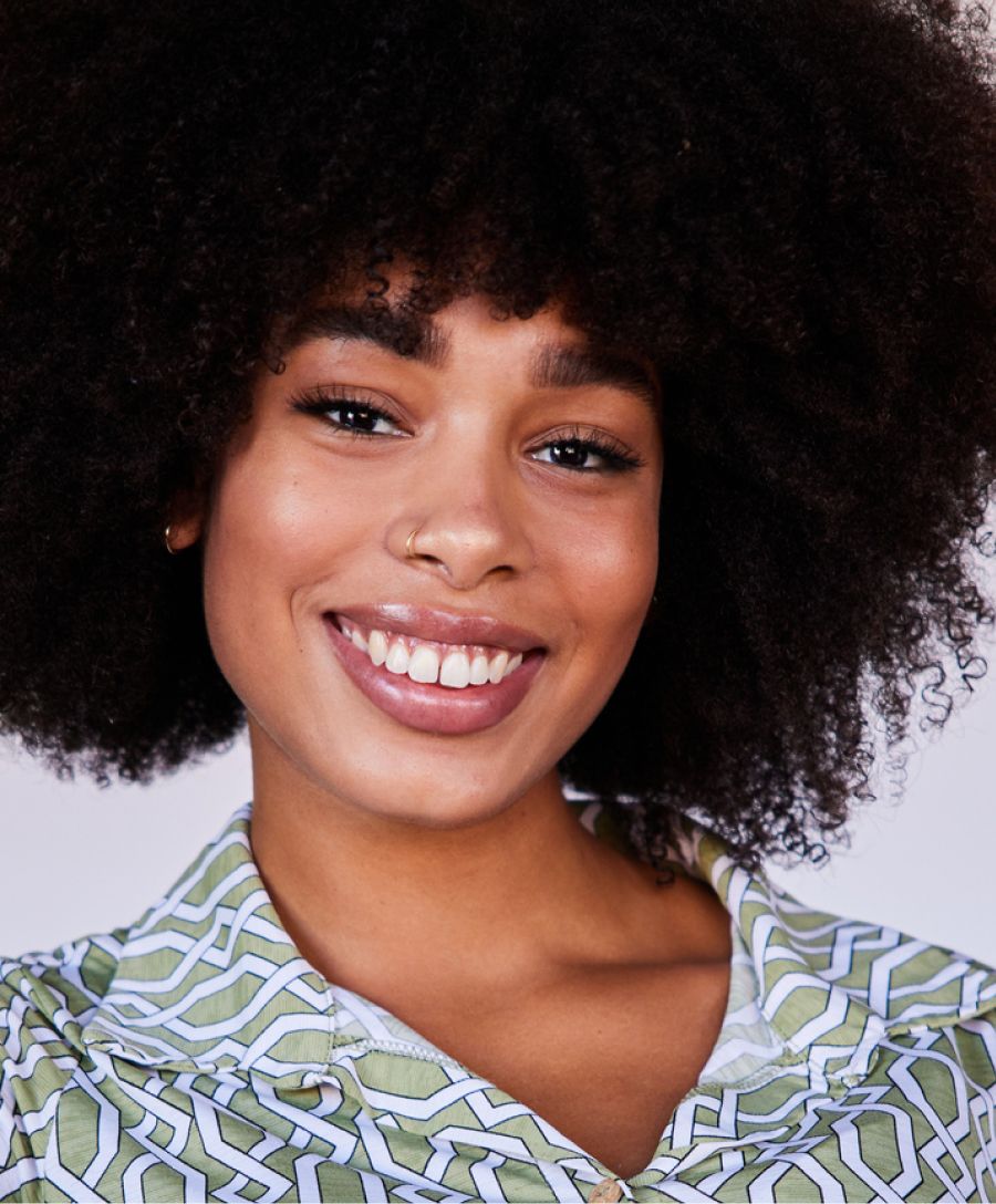 Smiling person with curly hair in patterned shirt.
