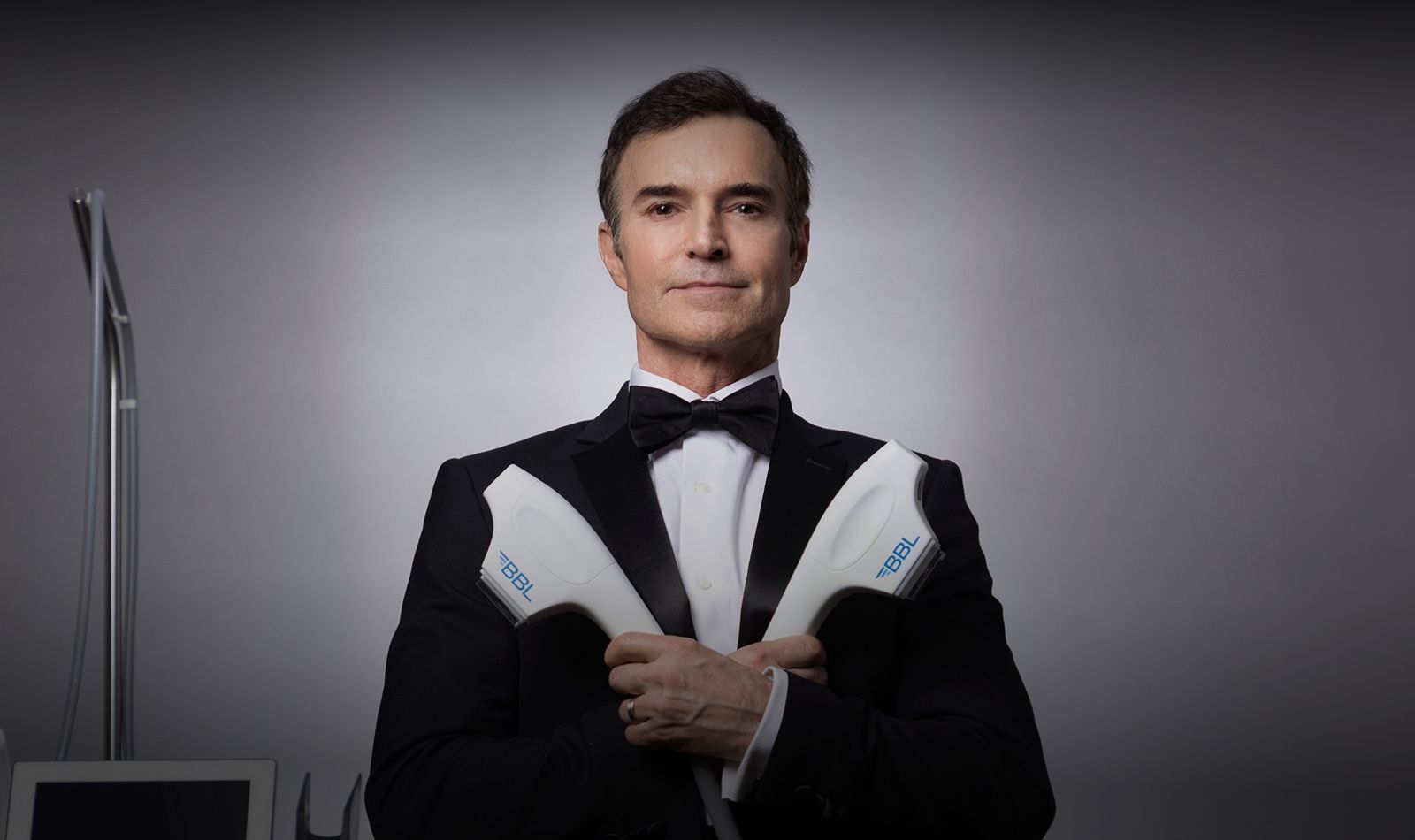 Man in tuxedo holding skincare equipment.