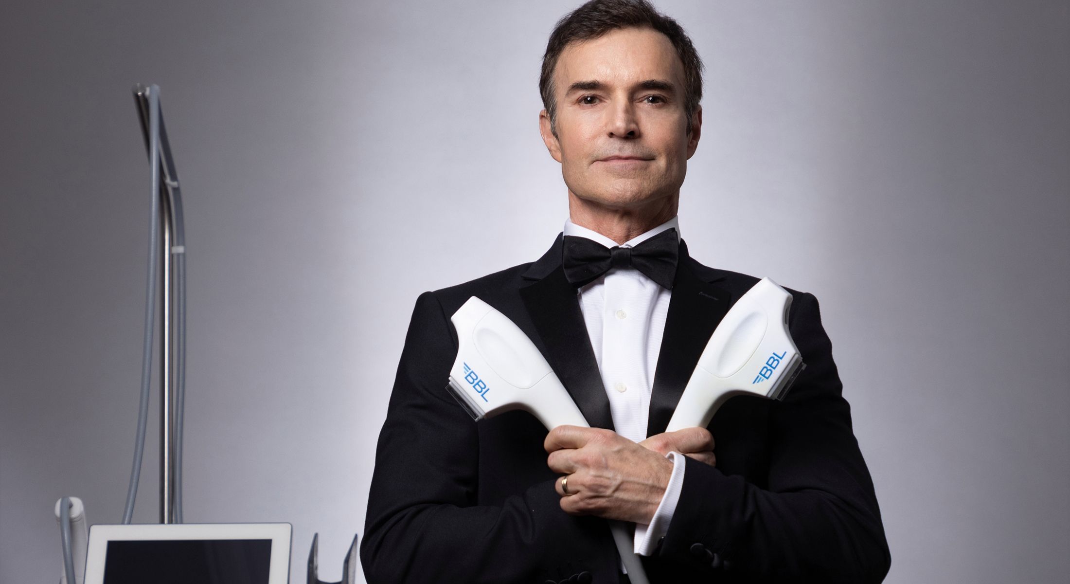 Man in tuxedo holding skincare equipment.
