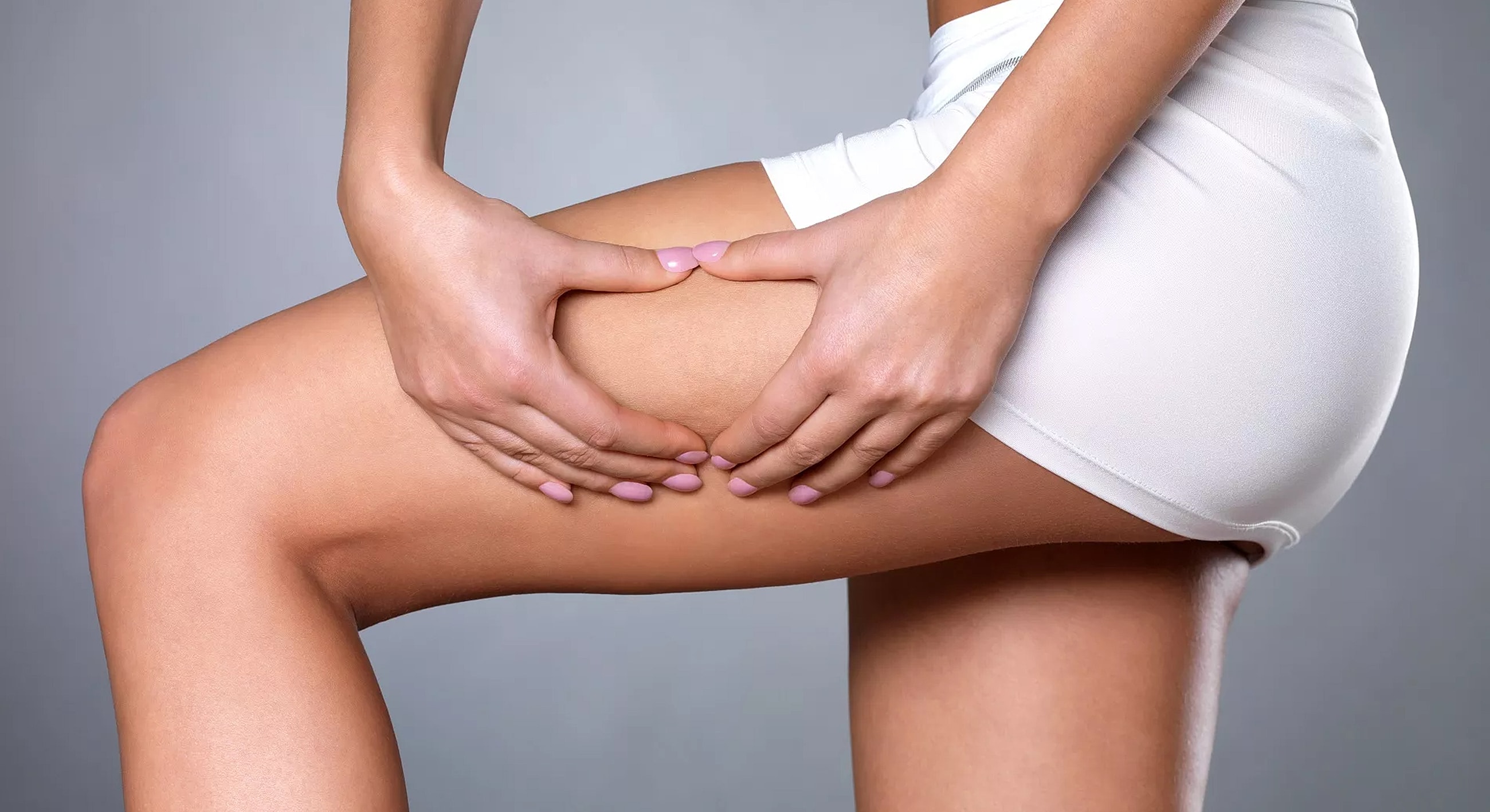 Woman assessing her thigh in white shorts.