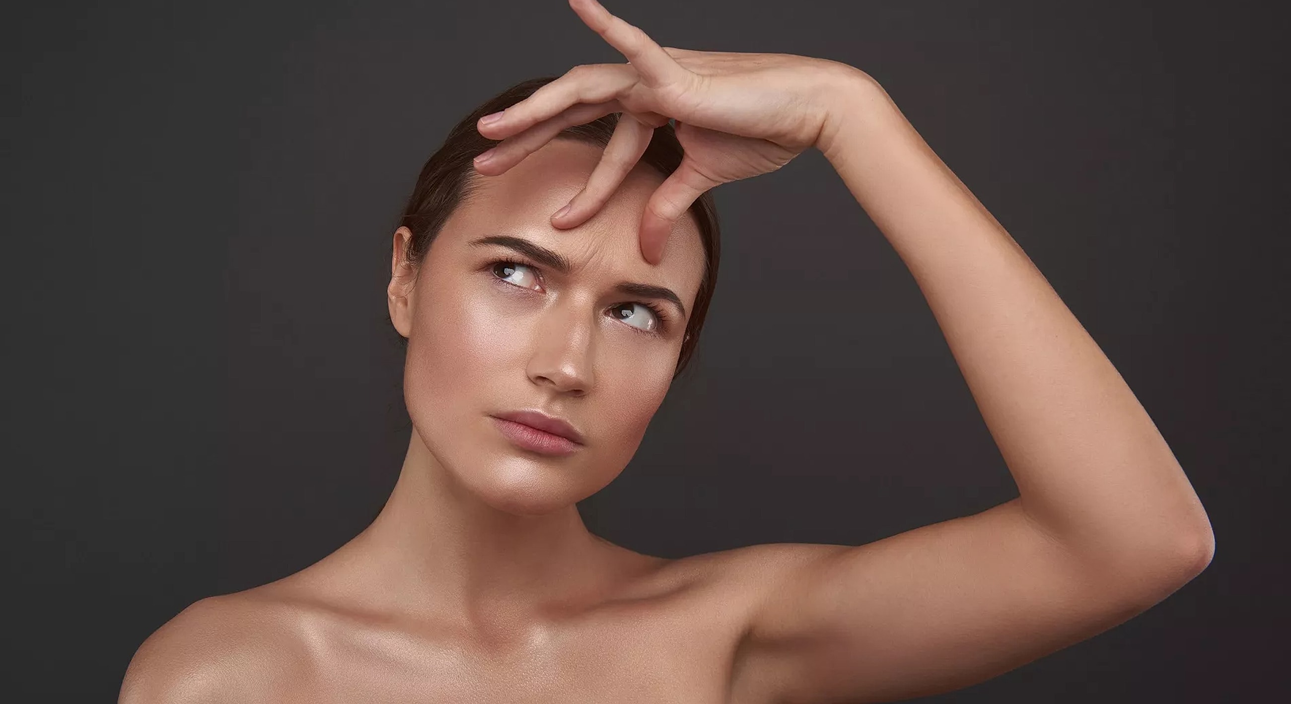 Woman thoughtfully touching her forehead against dark background.