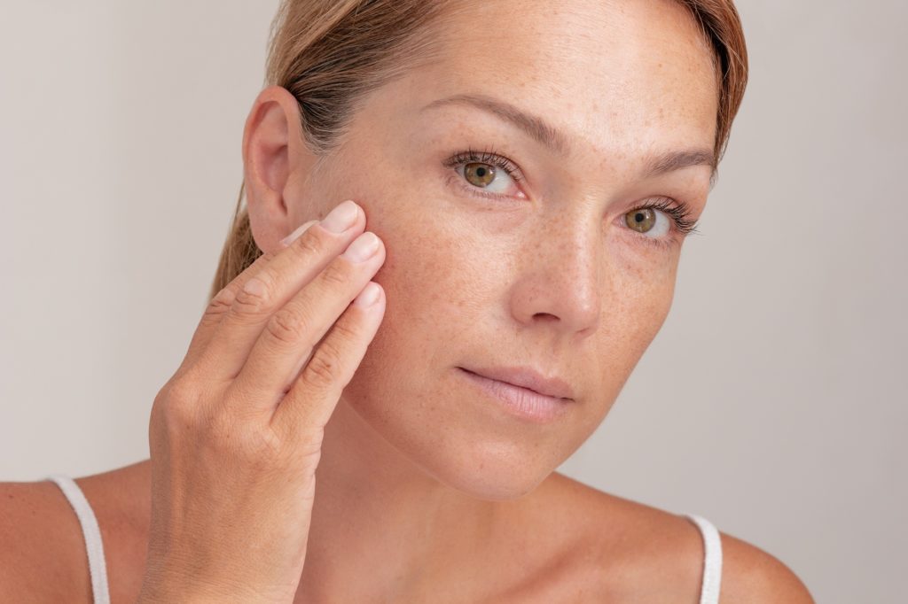 Woman with freckles on face touching skin