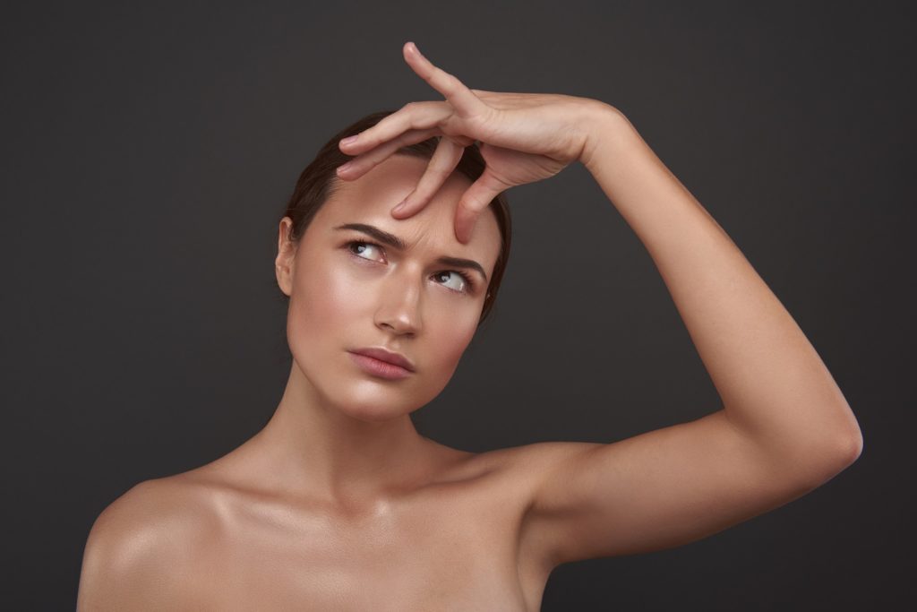 Beautiful young woman touching skin on her forehead and looking away