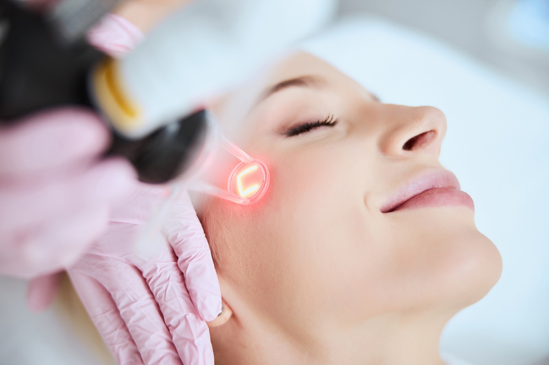Close up portrait of a young woman patient receiving a laser treatment in a spa salon. Calm pleased lady undergoing a cosmetic procedure | Patrick Bitter MD in Los Gatos, CA